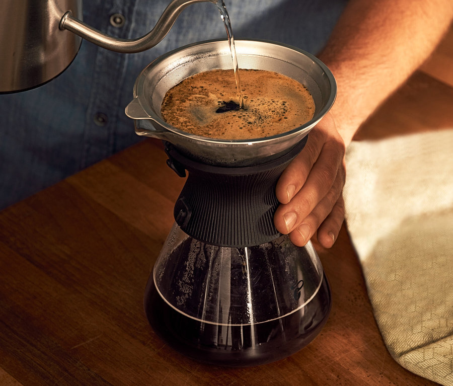 Adam, kahve filtresi olan BEEM Pour Over, 0,75 l cam sürahiye su döküyor.