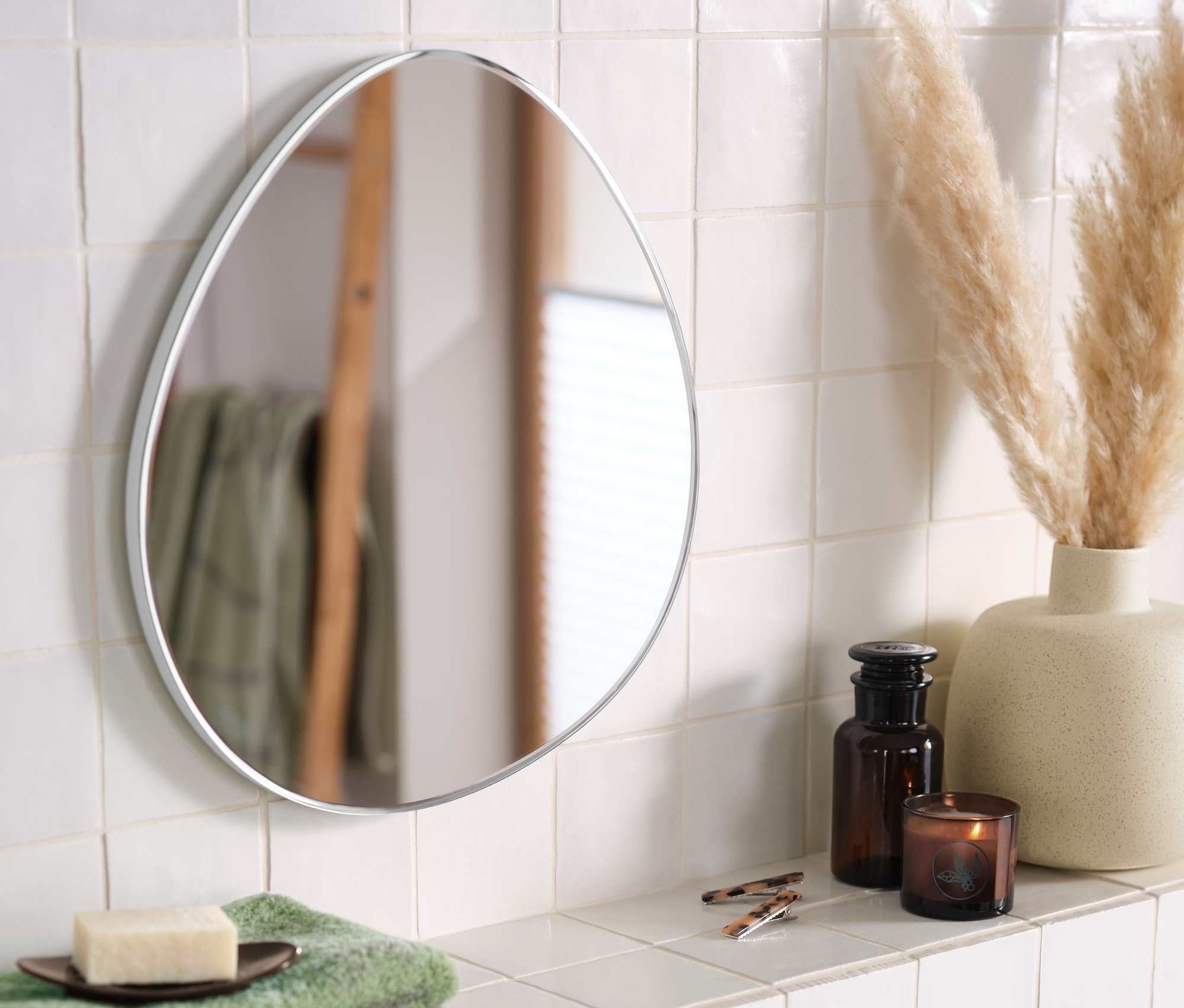 Beyaz bir rafta bir vazo ve organik şekilli bir duvar aynası duruyor.