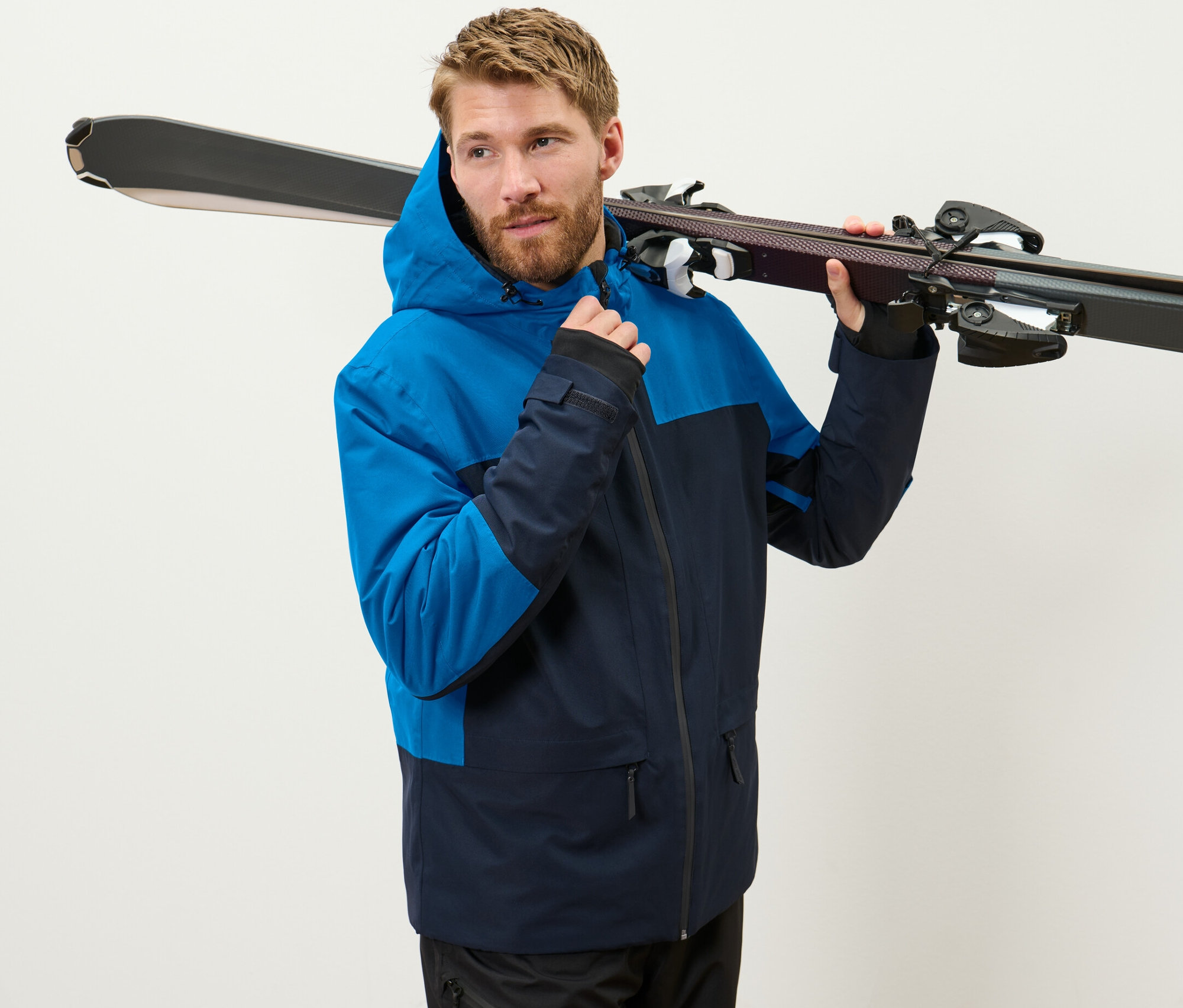 Mavi kayak montlu bir adam omzunda kayak taşıyor.