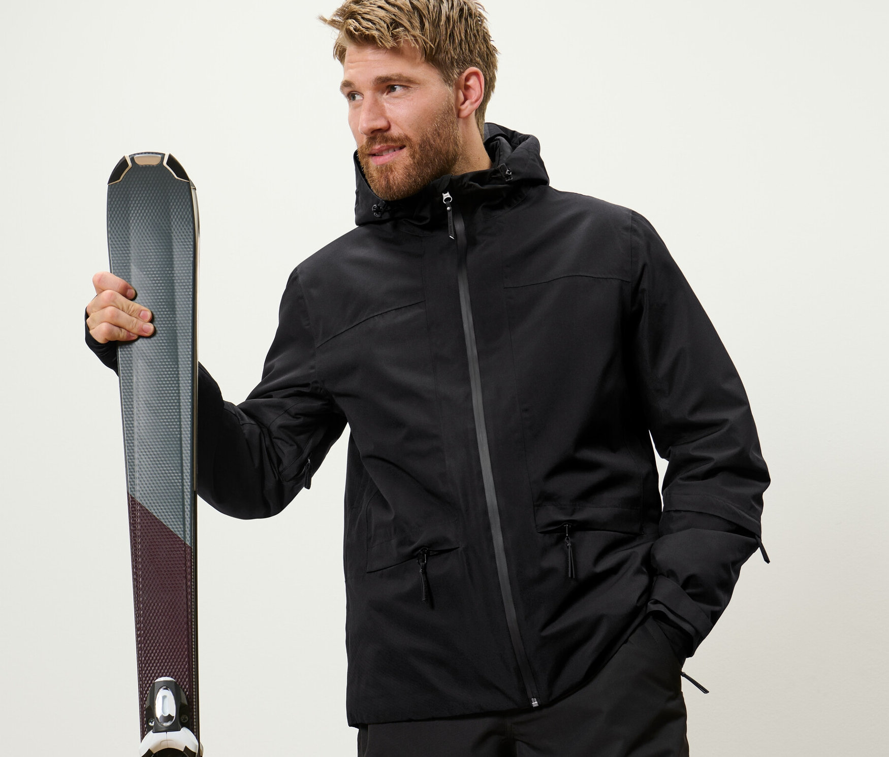 Kayak tutan bir adam. Siyah bir kayak montu giyiyor.