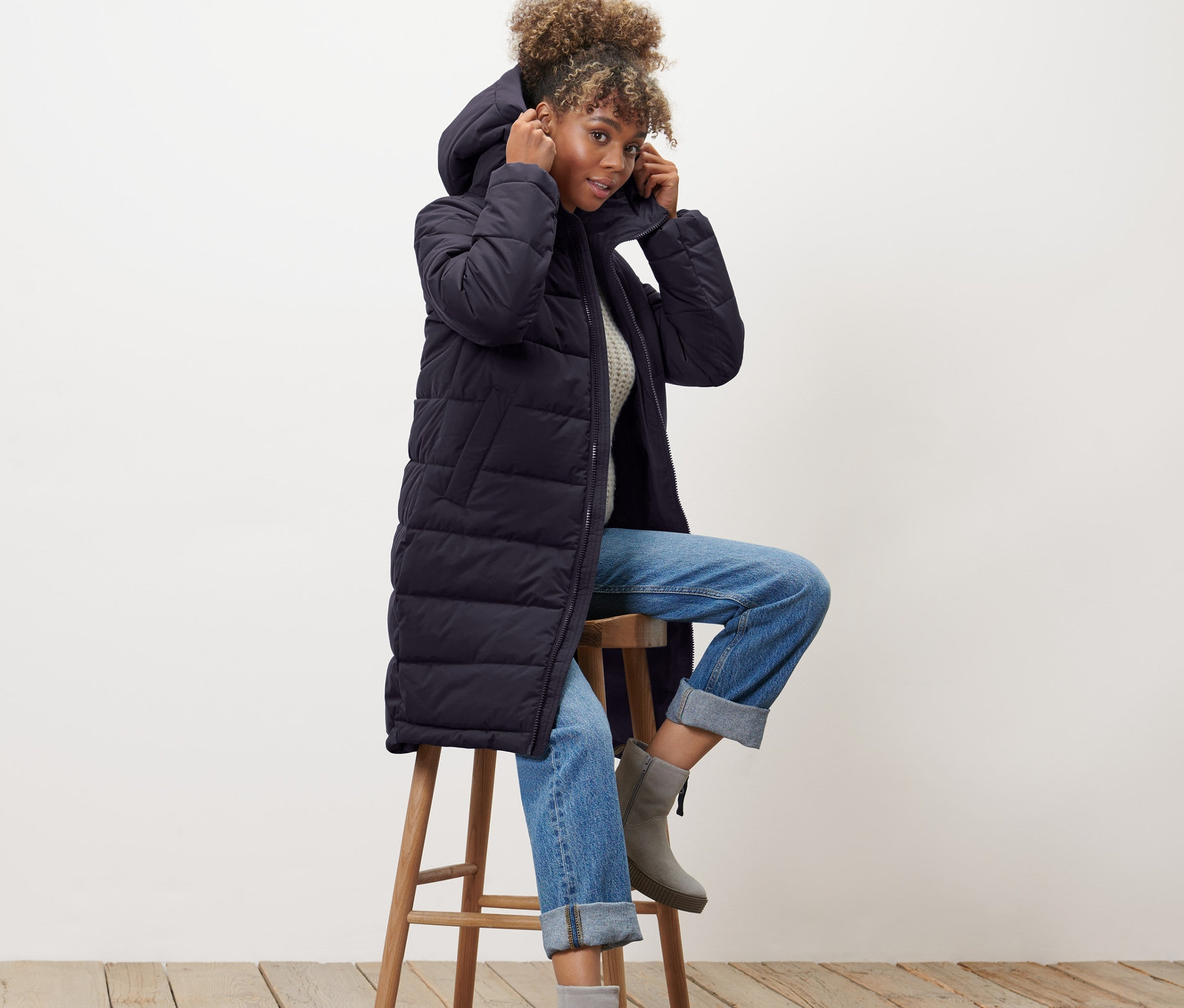 Kadın taburede oturuyor ve mavi kapitone mantosunun başlığını ayarlıyor.