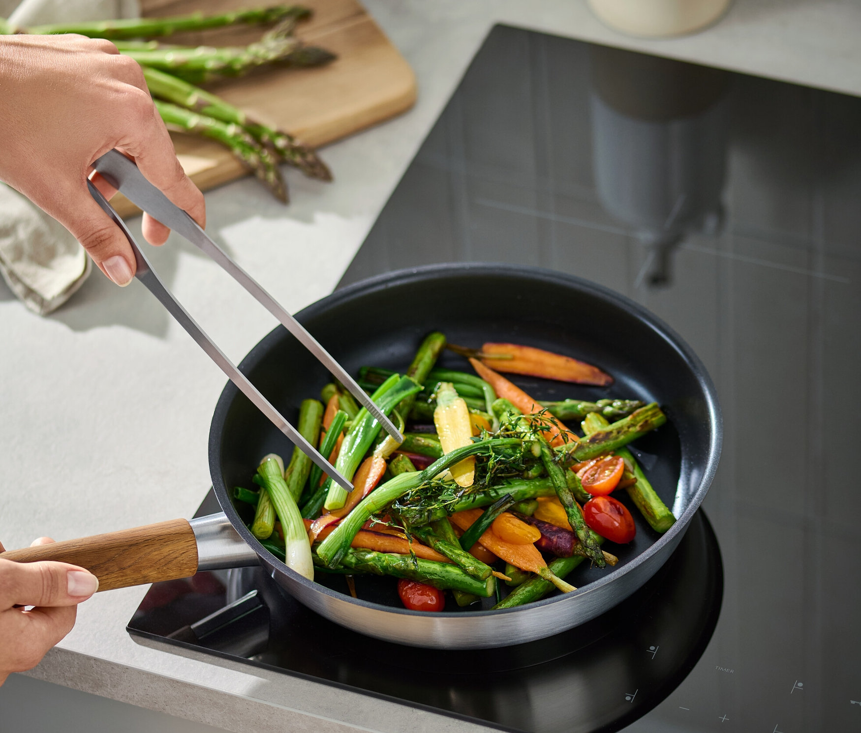 Bir kişi tavada sebzeleri karıştırmak için maşa kullanıyor.