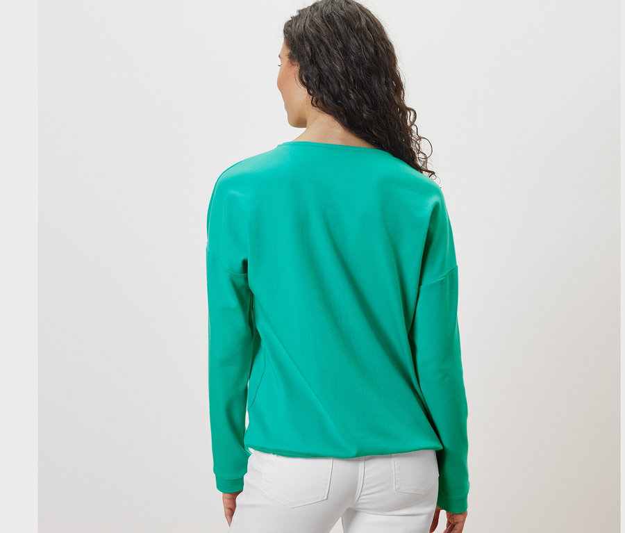 Arkadan, koyu saçlı bir kadının Deniz Mavisi renginde sweatshirt giydiği görülüyor.
