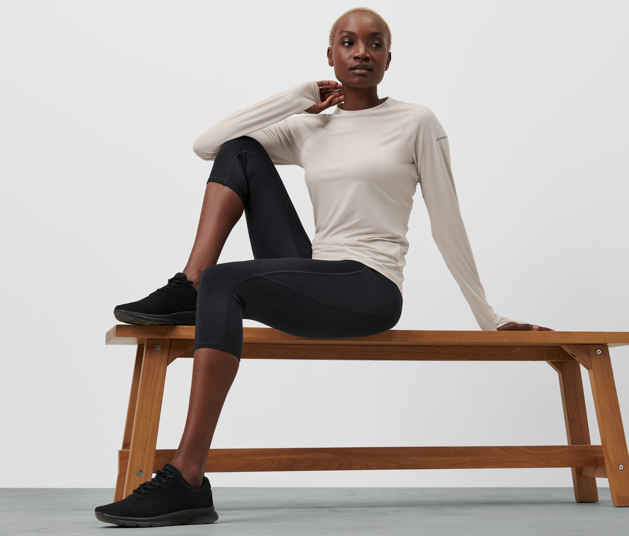 Kadın bankta oturuyor, siyah 3/4 spor taytı giyiyor.