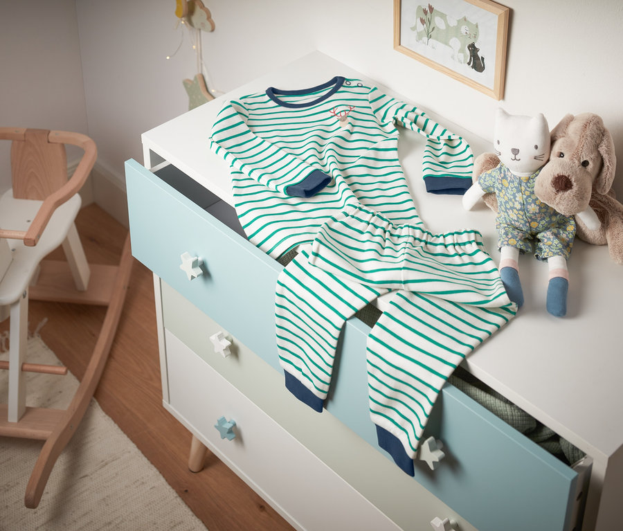 Çizgili organik pamuklu interlok pijama, oyuncakların yanında bir şifonyerin üzerinde duruyor.