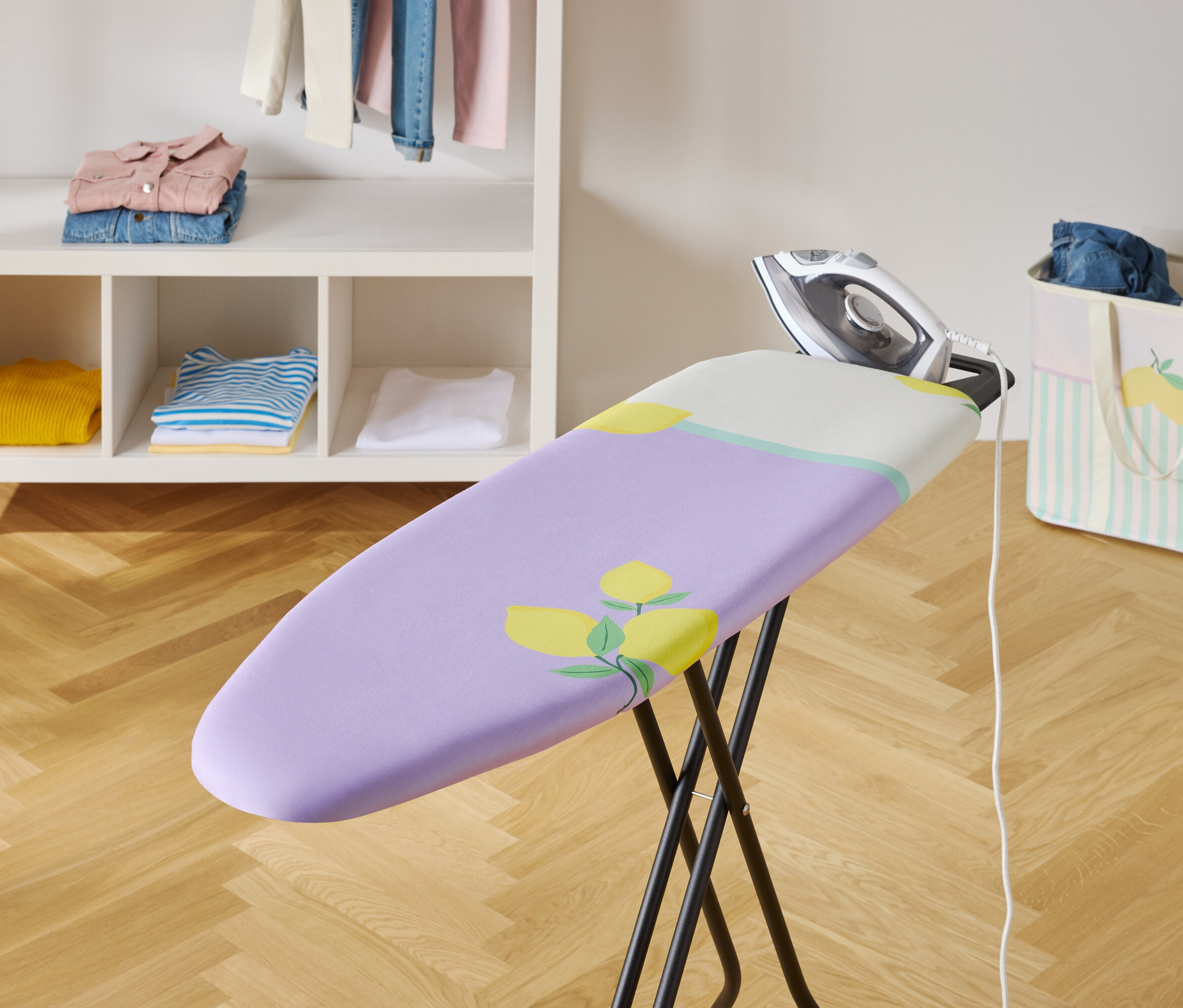 Ütü, mor örtülü ve çiçek desenli ütü masasının üzerinde.