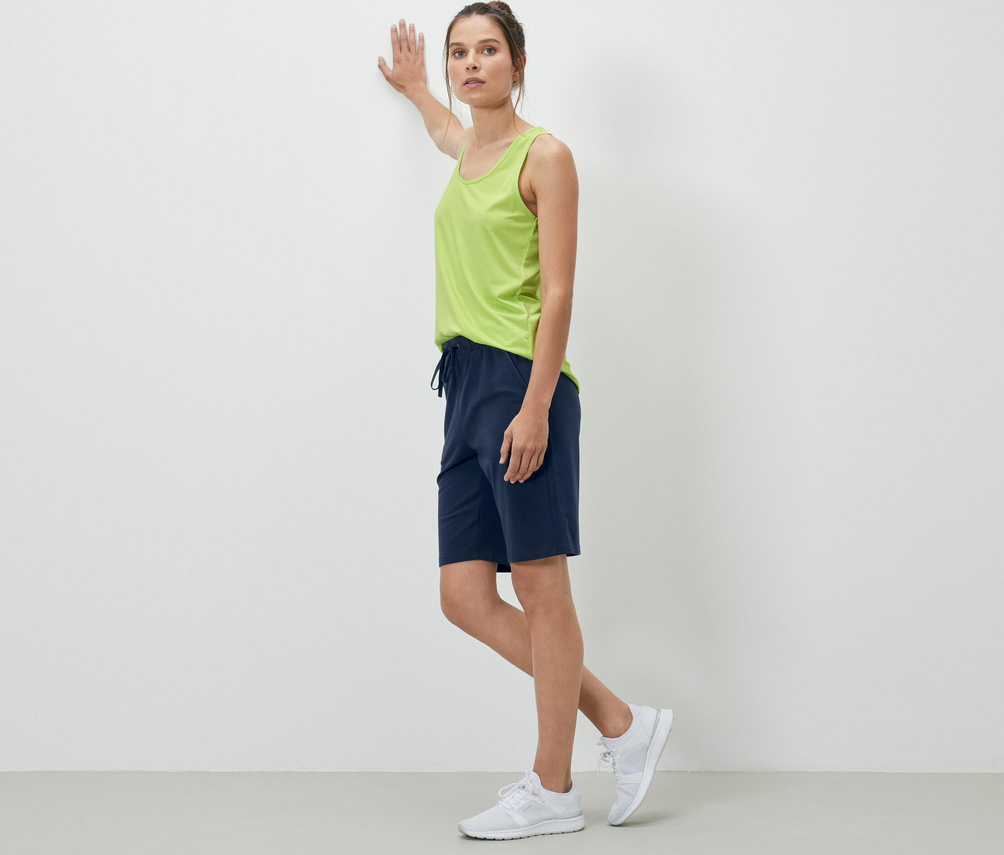 Duvara yaslanan kadın lacivert sweat şort giyiyor.