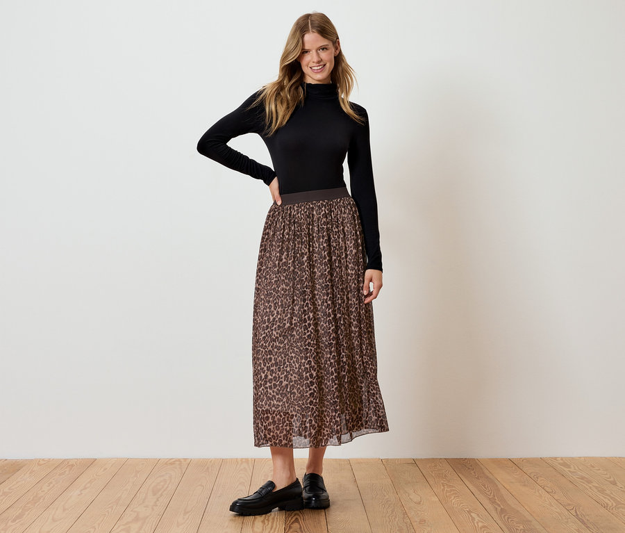 Kadın siyah balıkçı yaka bluz ve kahverengi leopar desenli etekle ayakta poz veriyor.