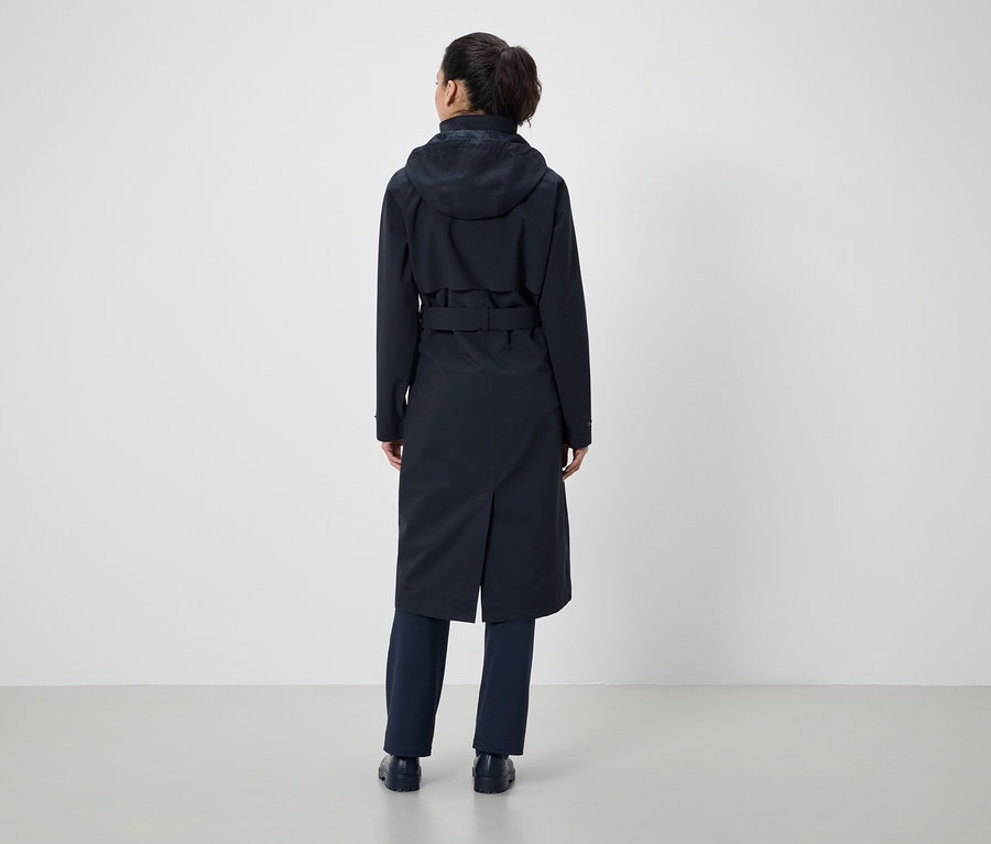 Arkadan at kuyruklu, koyu mavi kapüşonlu ve kemerli bir palto ve koyu mavi pantolon giyen bir kadın görülüyor.