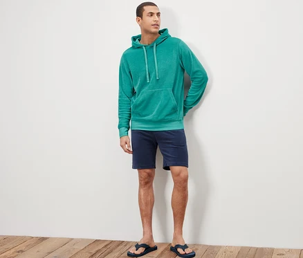 Adam ayakta duruyor ve Havlu Hoodie, şort ve parmak arası terlik giyiyor.