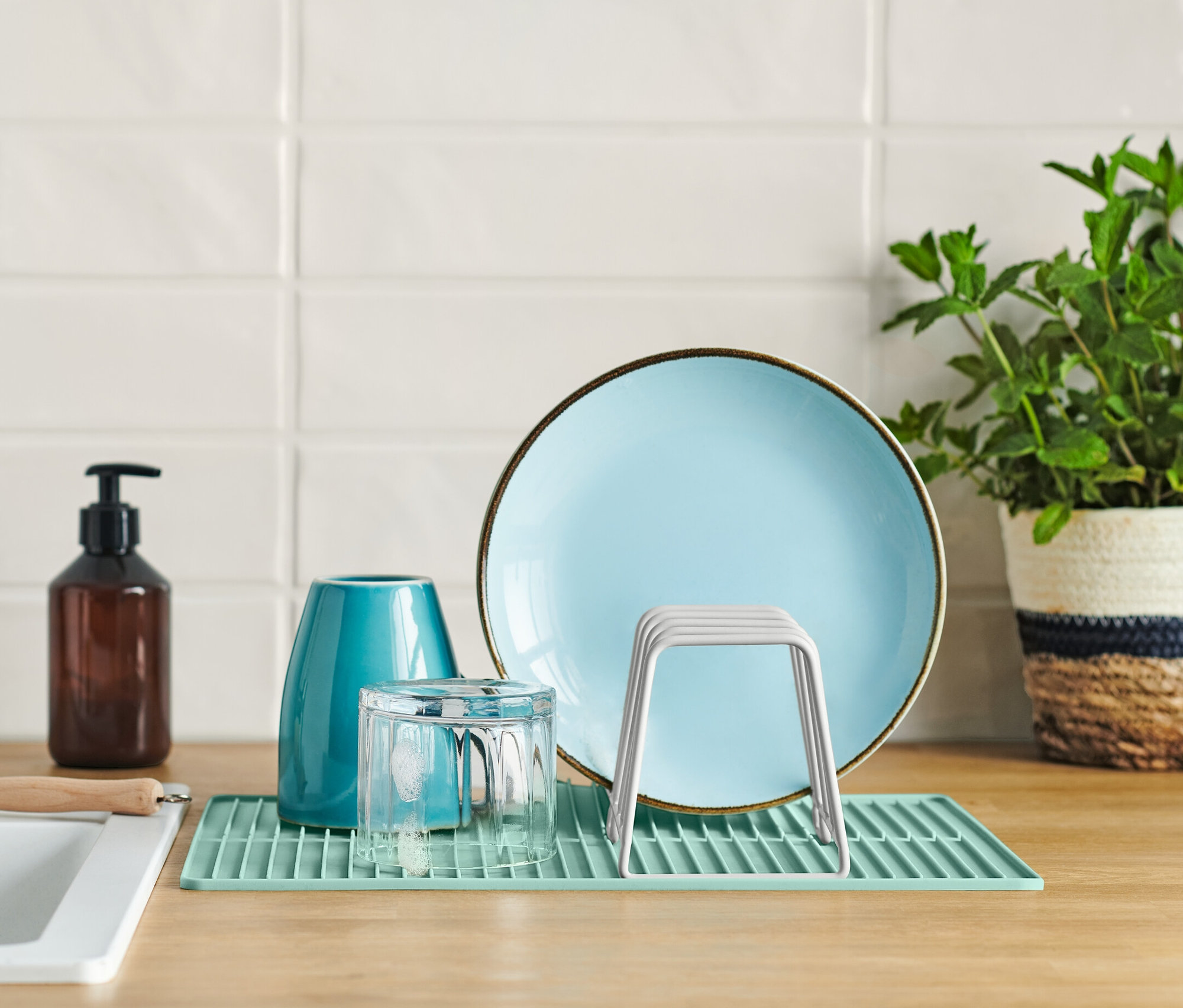Lavabonun yanında mutfak tezgahında mavi tabak, bardak ve silikon matlı bulaşık kurutma rafı