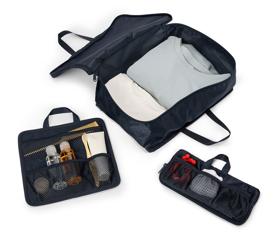 Saplı ve fermuarlı üç adet açık lacivert seyahat çantası beyaz bir zeminde sıralanmış. Çantaların içinde giysiler, kozmetik ürünleri ve aksesuarlar bulunmaktadır.