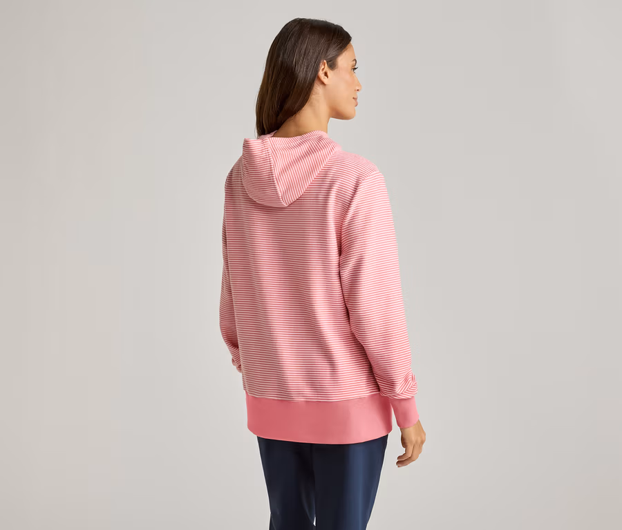 Omzunun üzerinden bakan bir kadın, pembe-beyaz çizgili kapüşonlu bir sweatshirt ve mavi pantolon giyiyor.