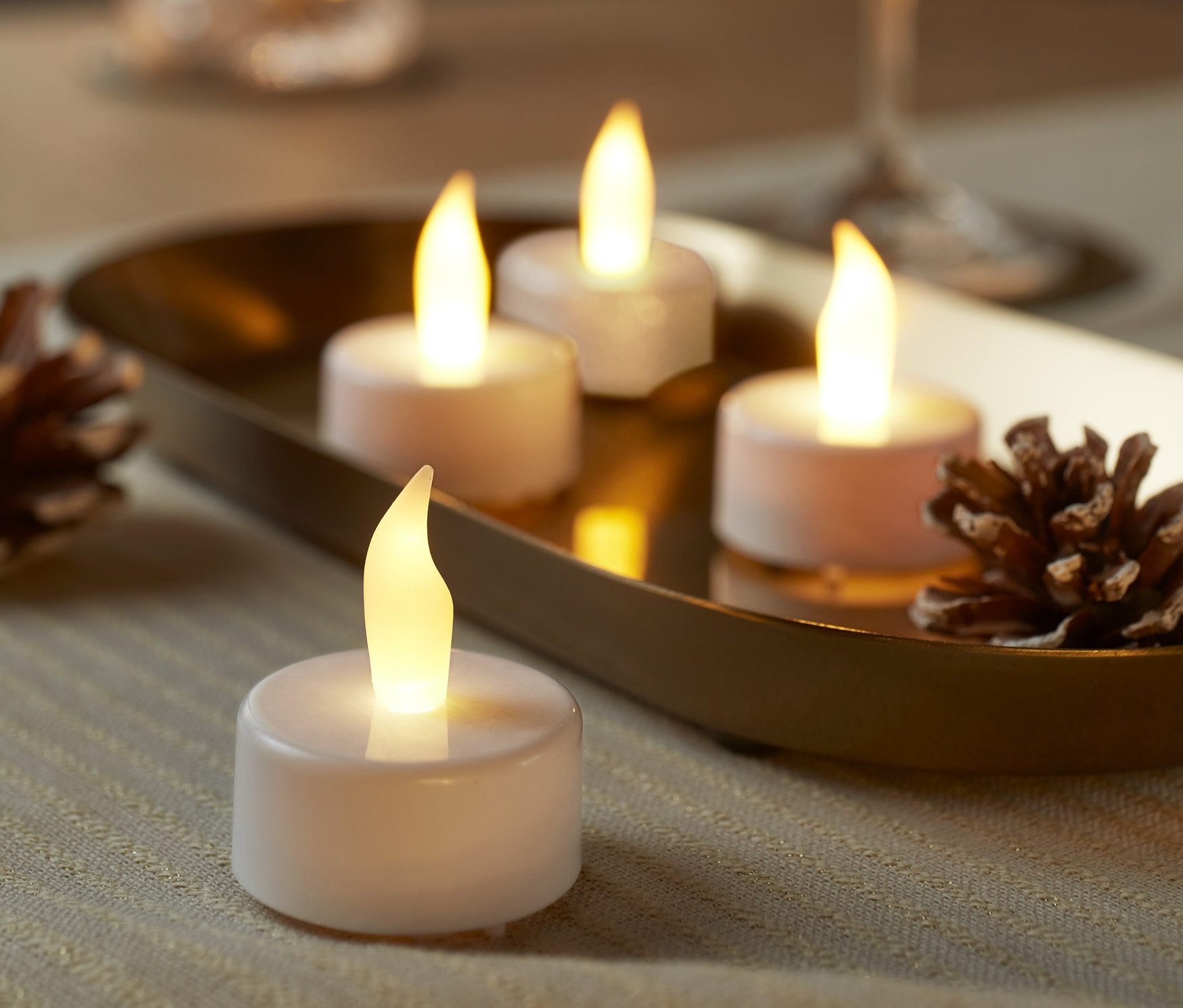 Kozalaklarla birlikte altın bir tepside dört adet beyaz LED Tealight Mum.