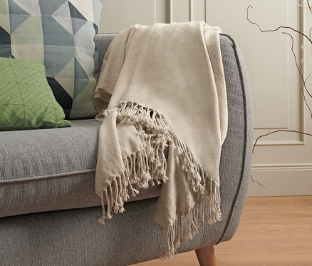 Bej şönil battaniye, yastıklı gri bir kanepenin üzerinde duruyor.