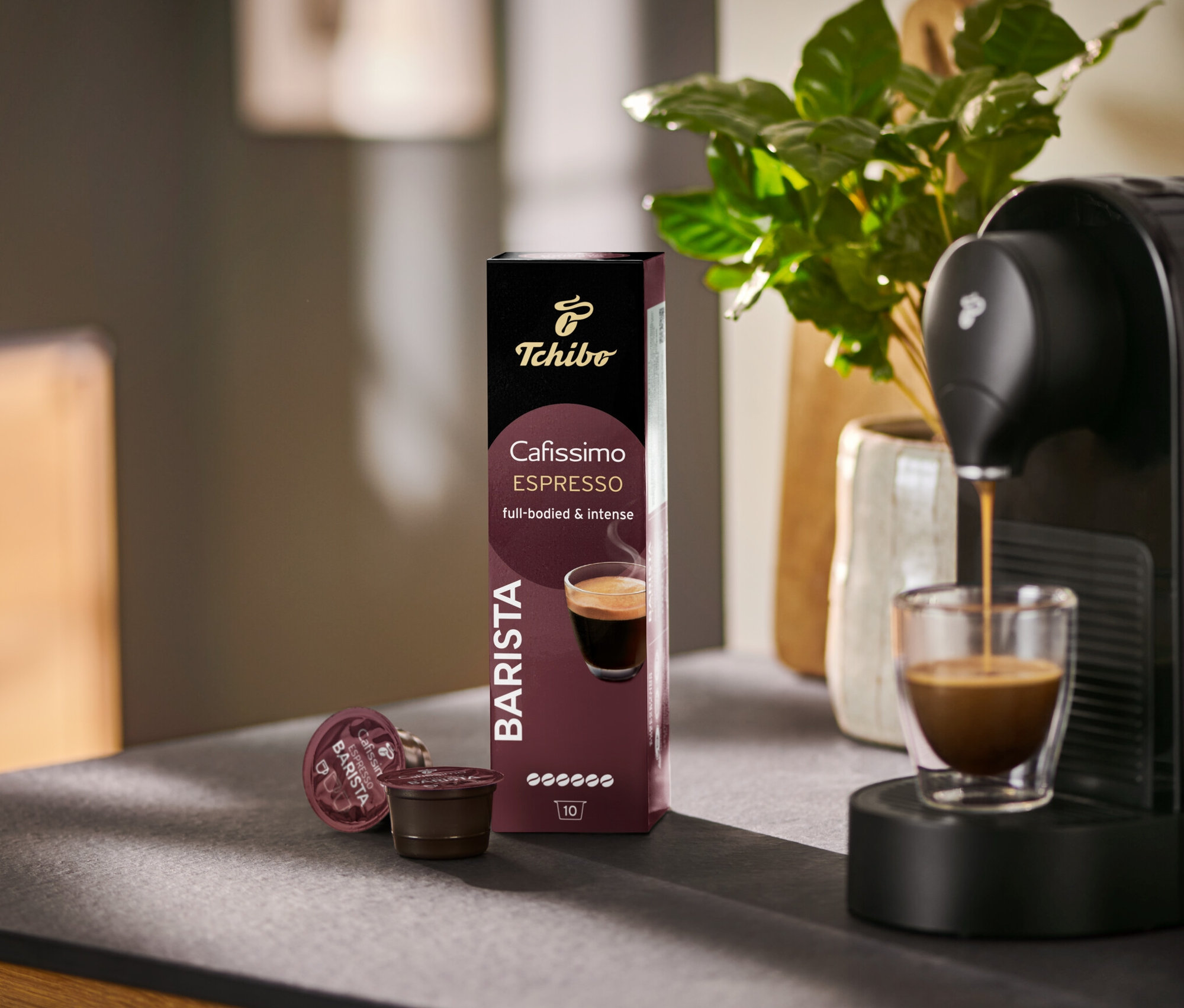 Bir Cafissimo BARISTA makinesinden bir bardağa espresso akıyor, yanında 10 kapsüllük bir paket.