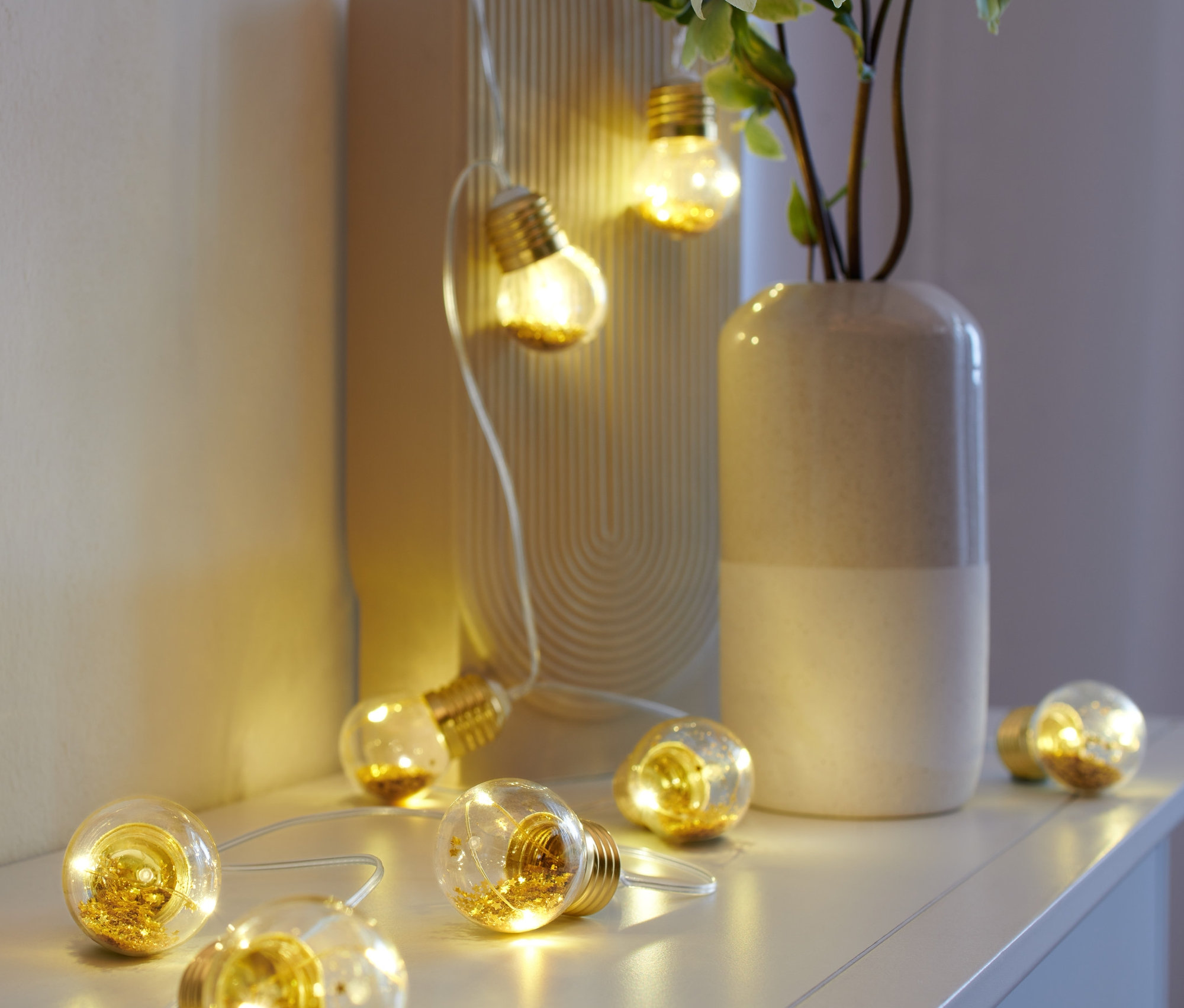 LED Ampul Işık Zinciri, beyaz bir rafta bir vazo ve resim çerçevesinin yanında duruyor.