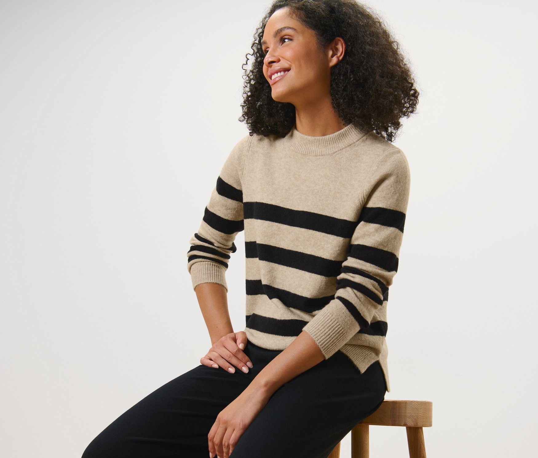 Kadın taburede oturuyor ve Çizgili Örgü Kazak giyiyor.