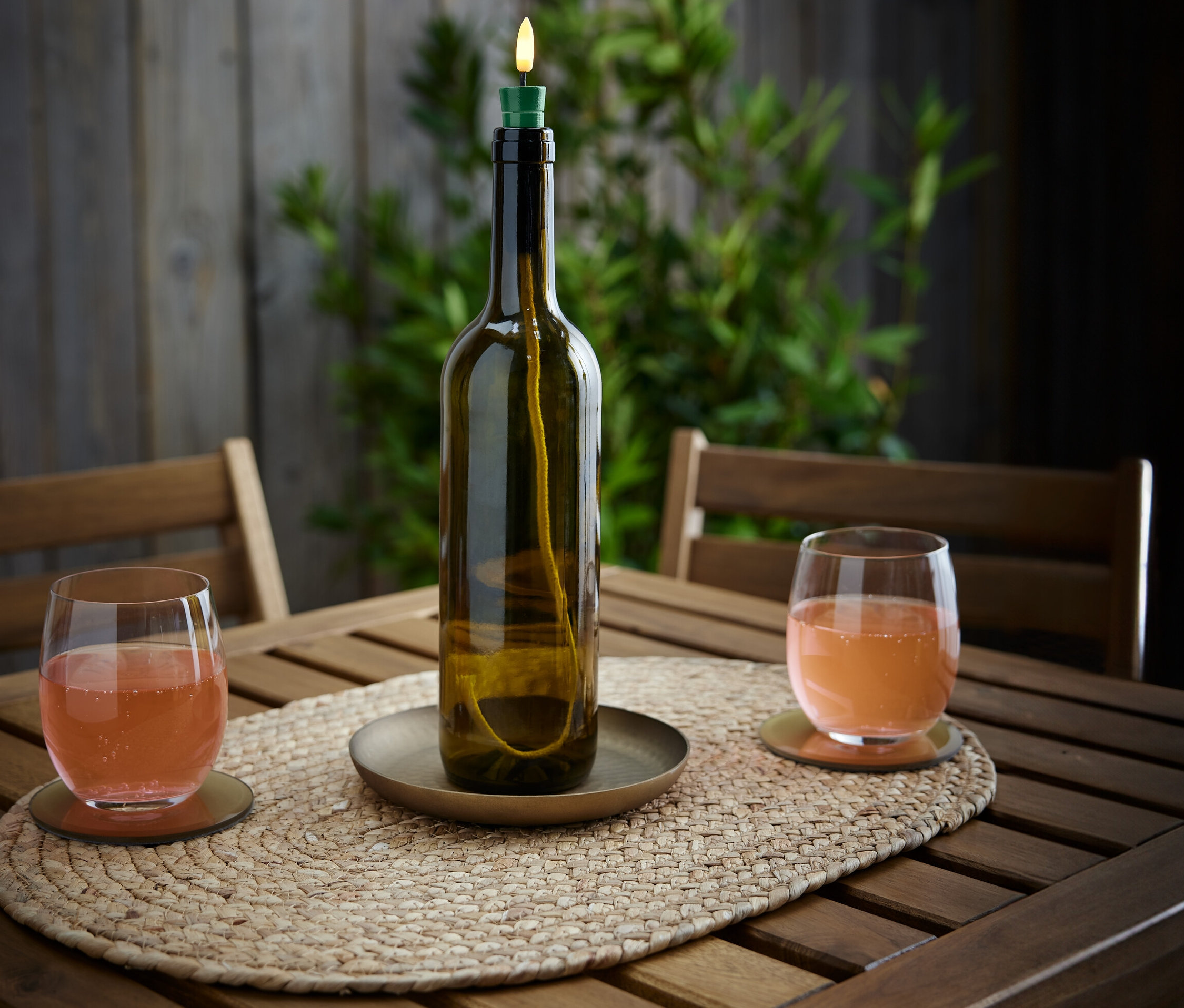 Ahşap bir masanın üzerinde bir LED Şişe Lambası »Candle« ve içinde içecek olan iki bardak duruyor.