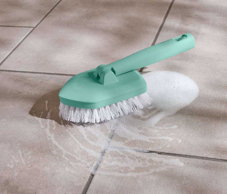 Turkuaz renkli, beyaz kıllı fırça, fayanslı bir zeminde bir köpük yığınının yanında duruyor.