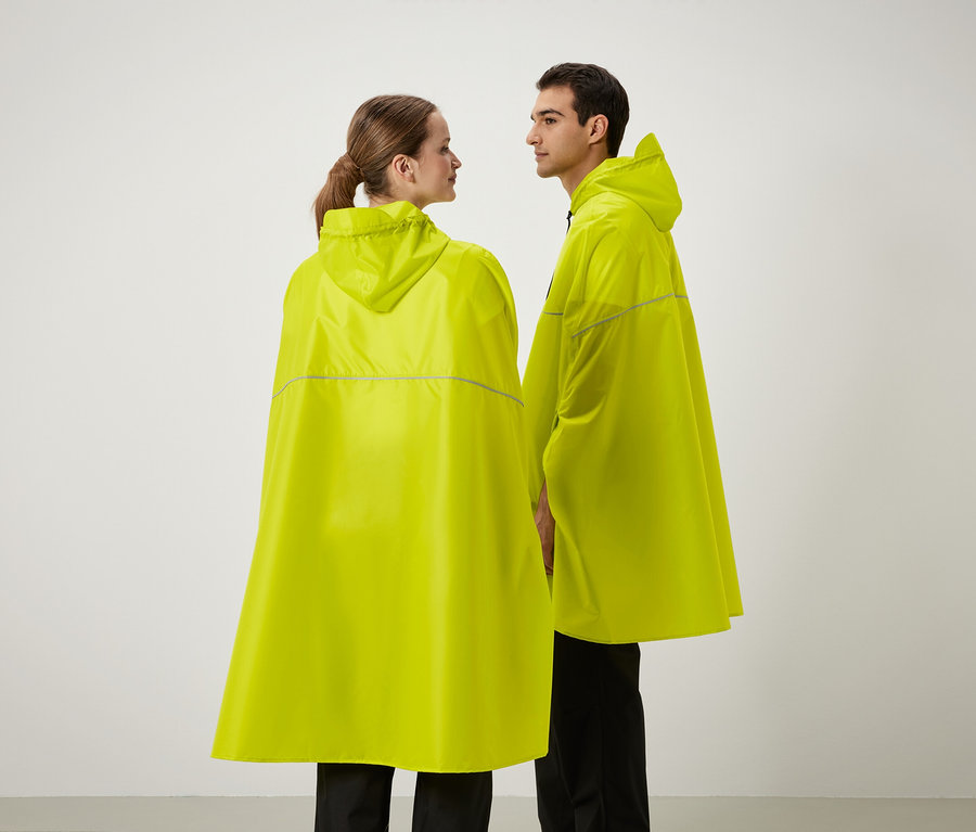 İki kişi yan yana duruyor, sarı renkli kapüşonlu yağmurluklar giyiyorlar.