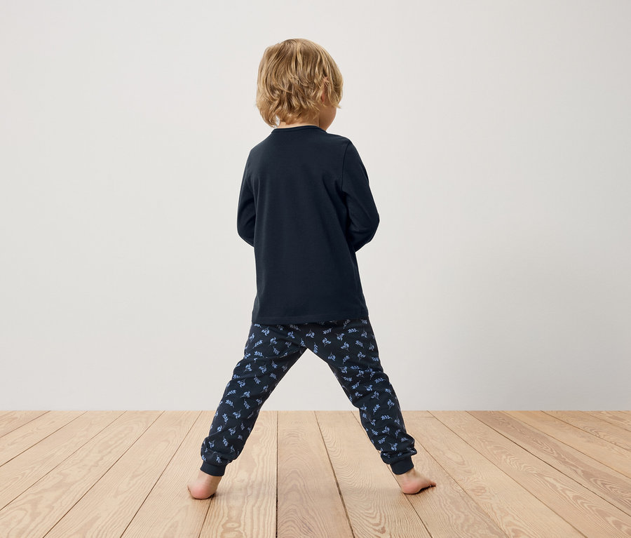 Arkadan görünüşlü erkek çocuk, lacivert uzun kollu pijama ve desenli pantolon giyiyor.
