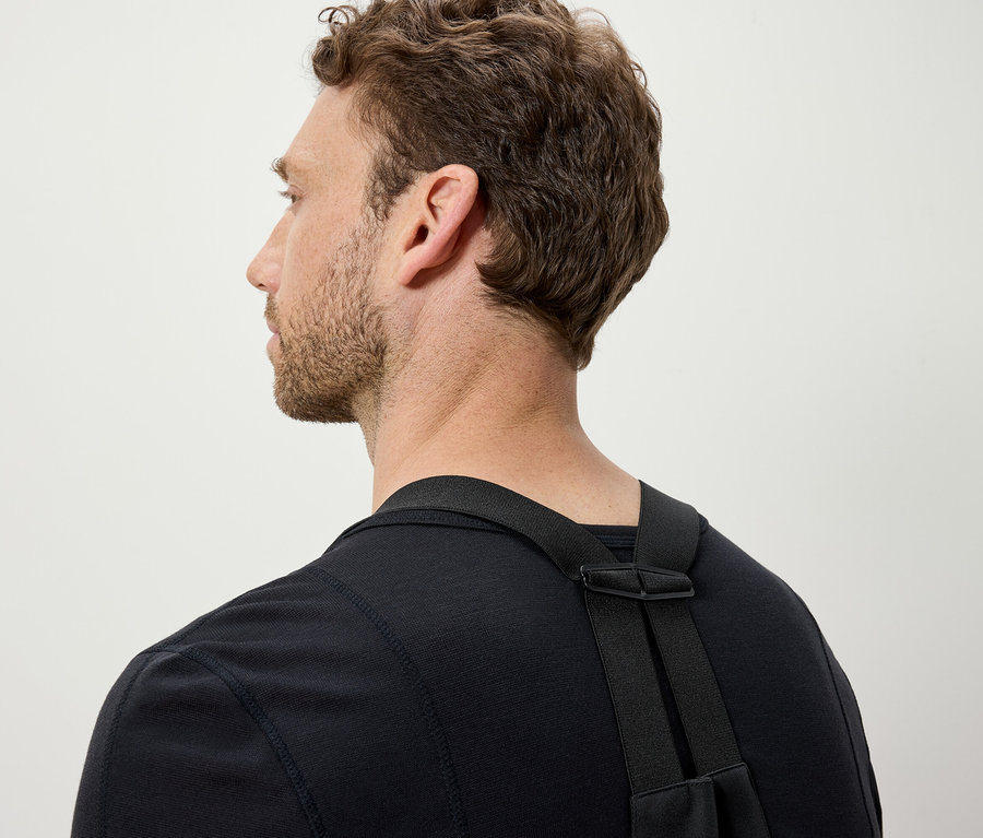 Kahverengi saçlı bir adam siyah bir tişört ve siyah askılar giyiyor.