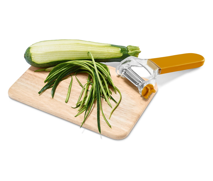 Tahta üzerinde yarım kabak, kabak şeritleri ve turuncu saplı bir soyucu var.