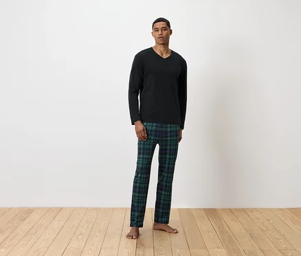 Siyah uzun kollu tişört ve yeşil ekose pijama altı giyen bir adam ayakta duruyor.