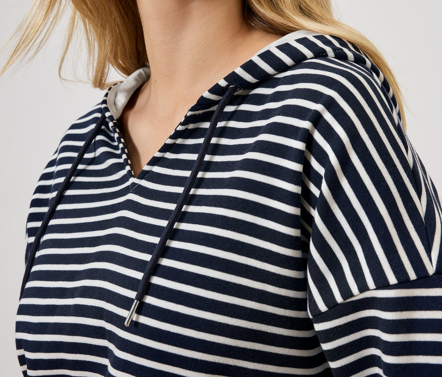 Sarışın bir kadın, mavi beyaz çizgili kapüşonlu bir sweatshirt giyiyor.