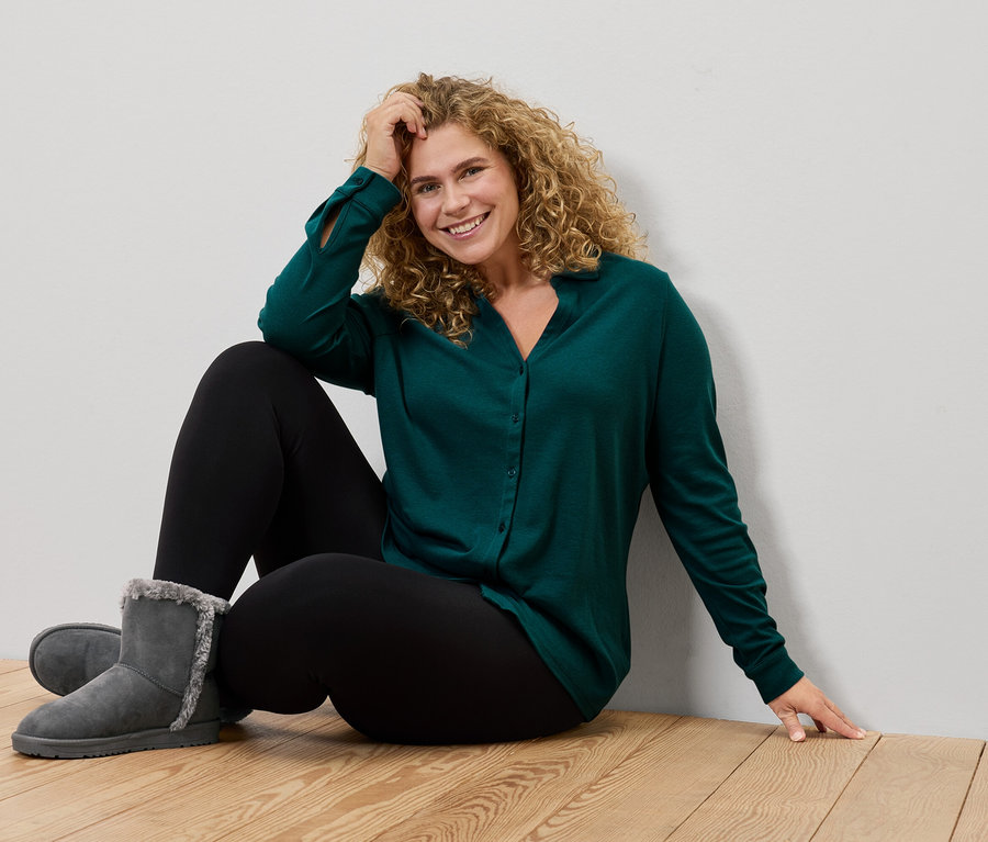 Kadın yerde oturuyor, yeşil gömlek, siyah tayt ve gri botlar giyiyor.