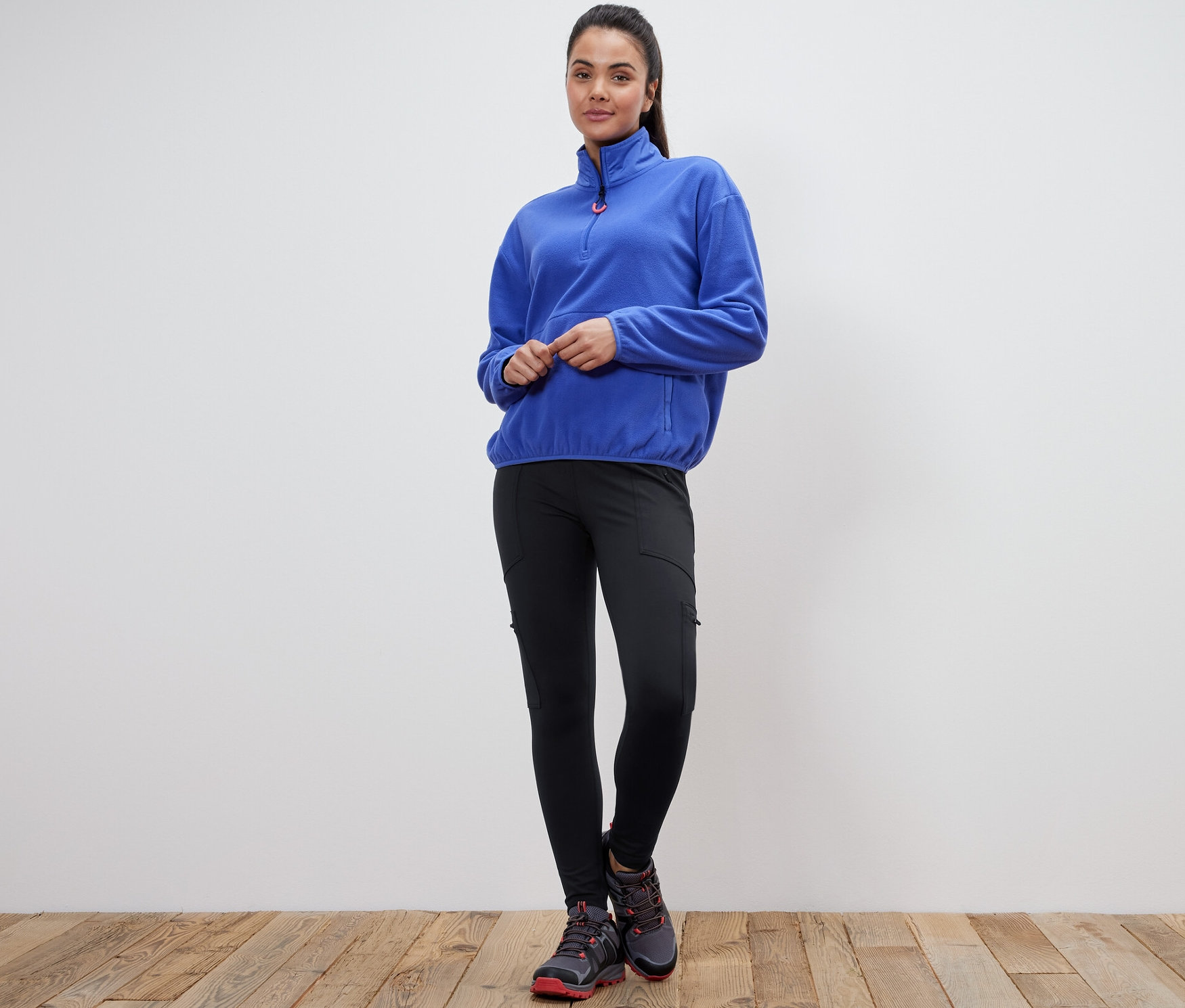 Kadın ayakta duruyor, mavi polar bir kazak ve siyah bir Outdoor Taytı giyiyor.