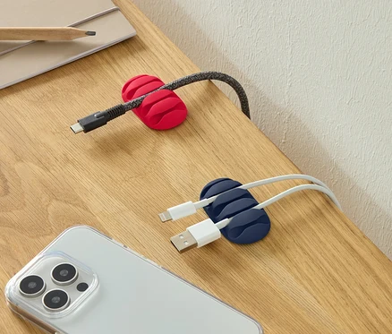 Kırmızı kablo tutucuda bir USB-C kablosu, mavi kablo tutucuda iki USB kablosu ve bir masa üzerinde akıllı telefon.