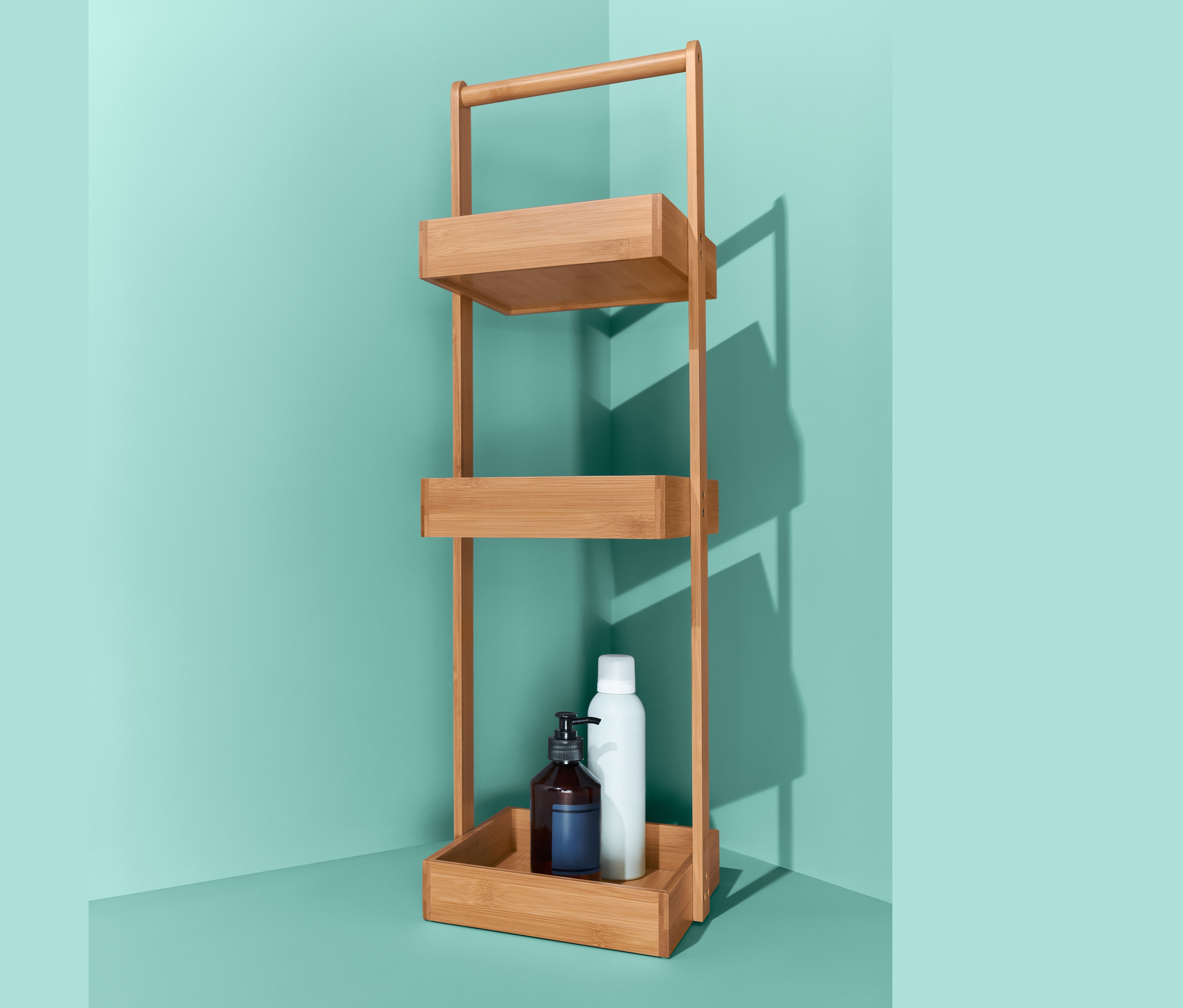 Üç raflı bambu rafın en alt rafında pompalı kahverengi bir şişe ve beyaz bir şişe bulunmaktadır.