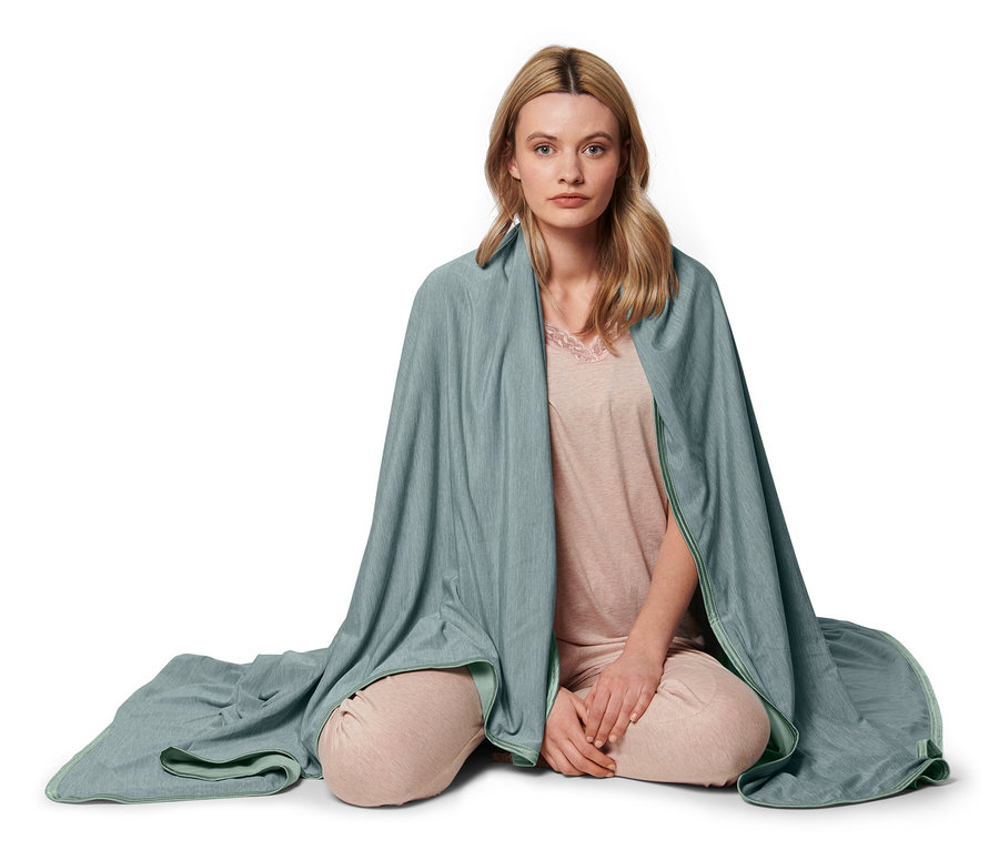 Kadın bağdaş kurmuş oturuyor ve serinletici bir battaniyeye sarılmış.