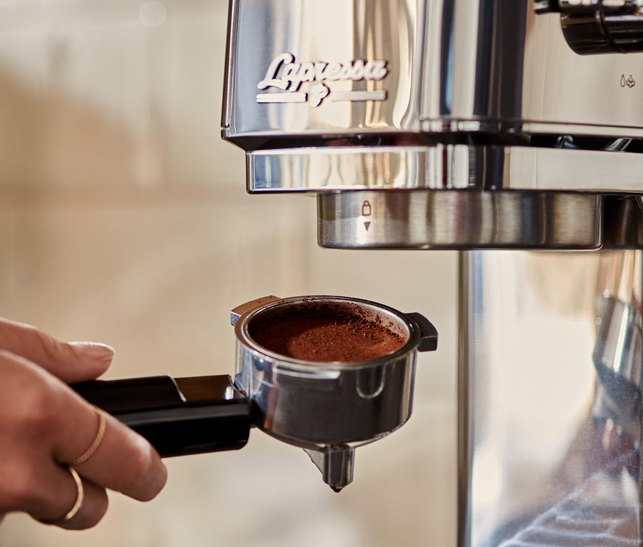 Kadın, kahveyle dolu gümüş renkli »Lapressa« Portafiltre Makinesini kahve makinesine yerleştiriyor.