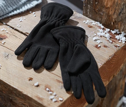 Siyah mikro polar eldivenler, gri örgü bir şapkanın yanında ahşap bir bankta duruyor.