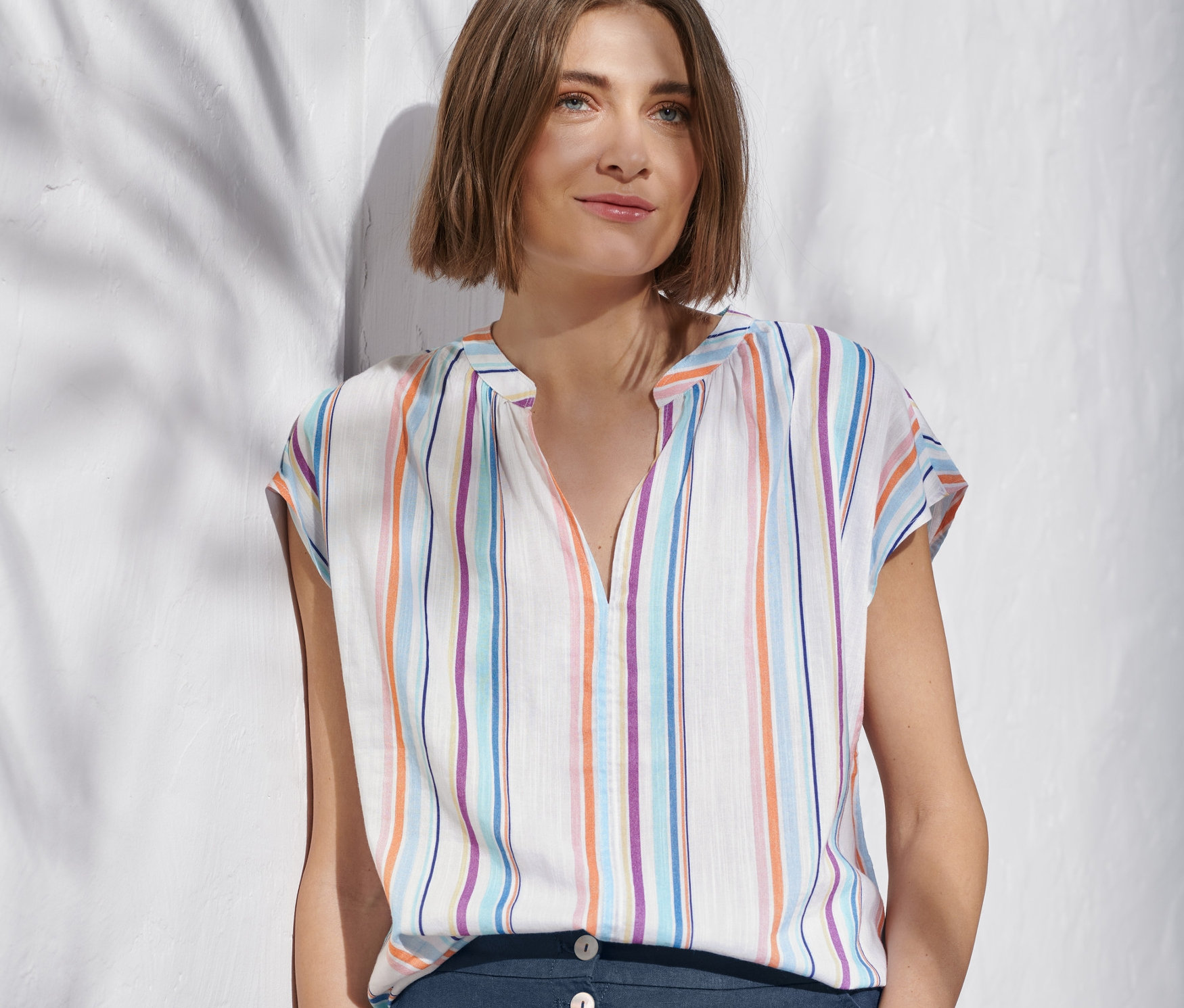 Duvara yaslanmış bir kadın, Organik Pamuklu Çizgili Dokuma Bluz ve lacivert pantolon giyiyor.