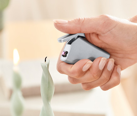 Bir kadın elektrikli çakmak ile bir mum yakıyor.