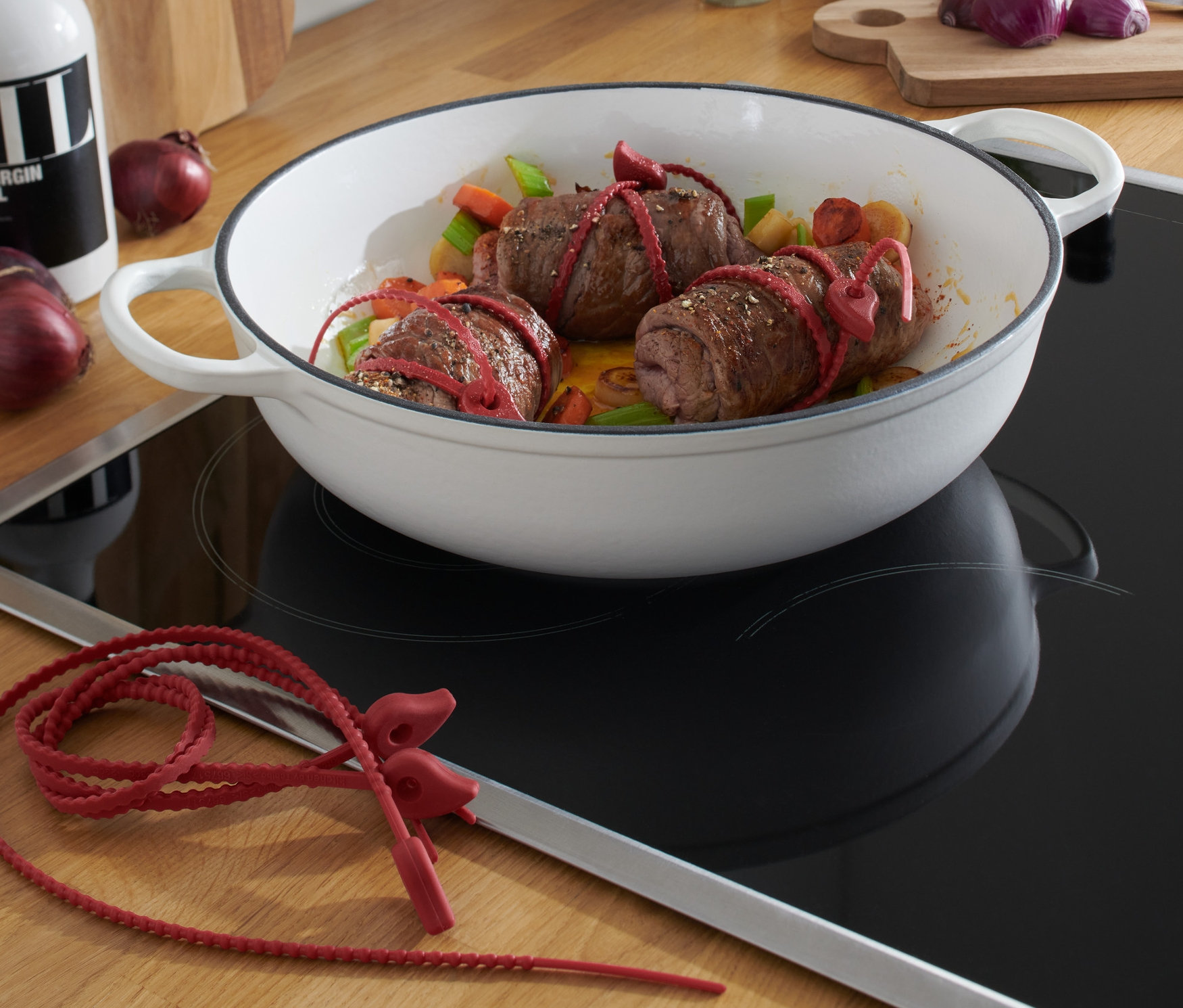 Beyaz bir tavada 6 Adet Silikon Şerit ile bağlanmış üç etli rulo yemeği. 