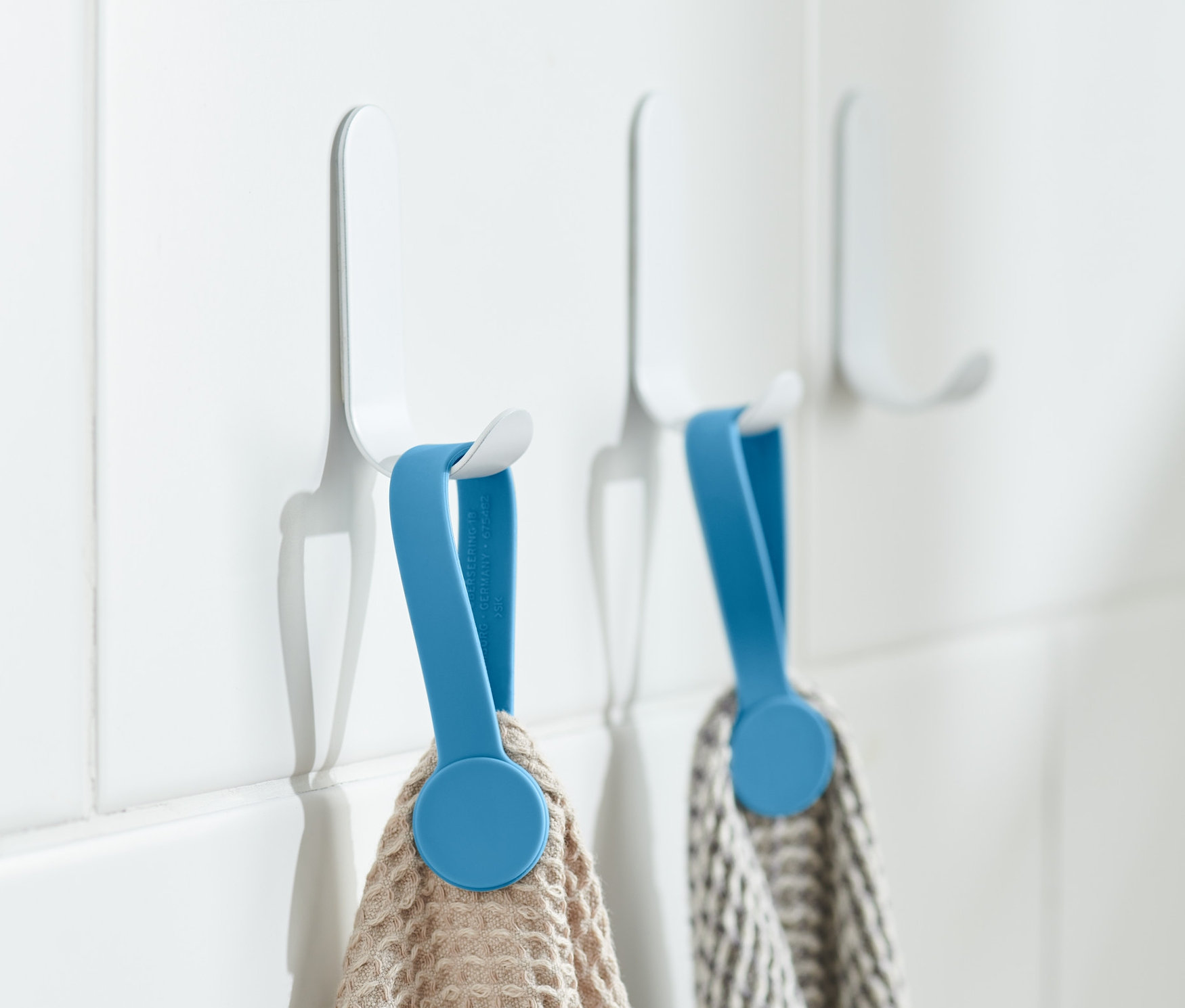 İki havlu, beyaz fayanslar üzerinde beyaz kancalarda mavi 2 Adet Manyetik Klips ile asılı duruyor.