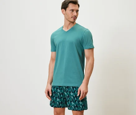 Adam kısa kollu ve desenli şortlu bir şortlu pijama takımı giyiyor.