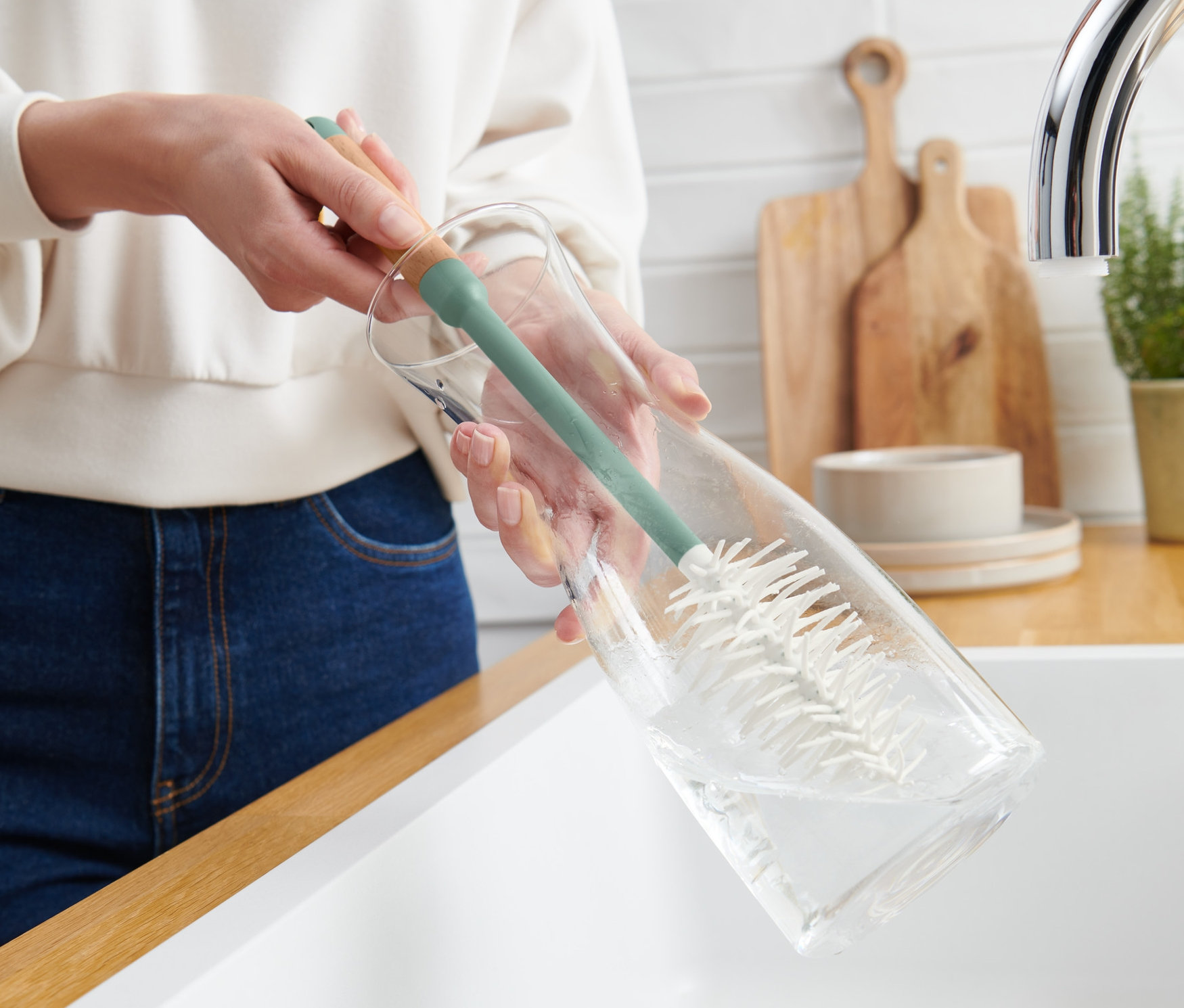 Bir kadın, Bardak ve Şişe Temizleme Fırçası ile cam bir şişeyi temizliyor.