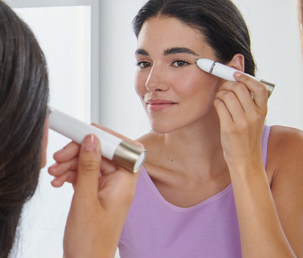 Kadın aynanın önünde Elektrikli Kaş Şekillendirici ile kaşlarını şekillendiriyor.