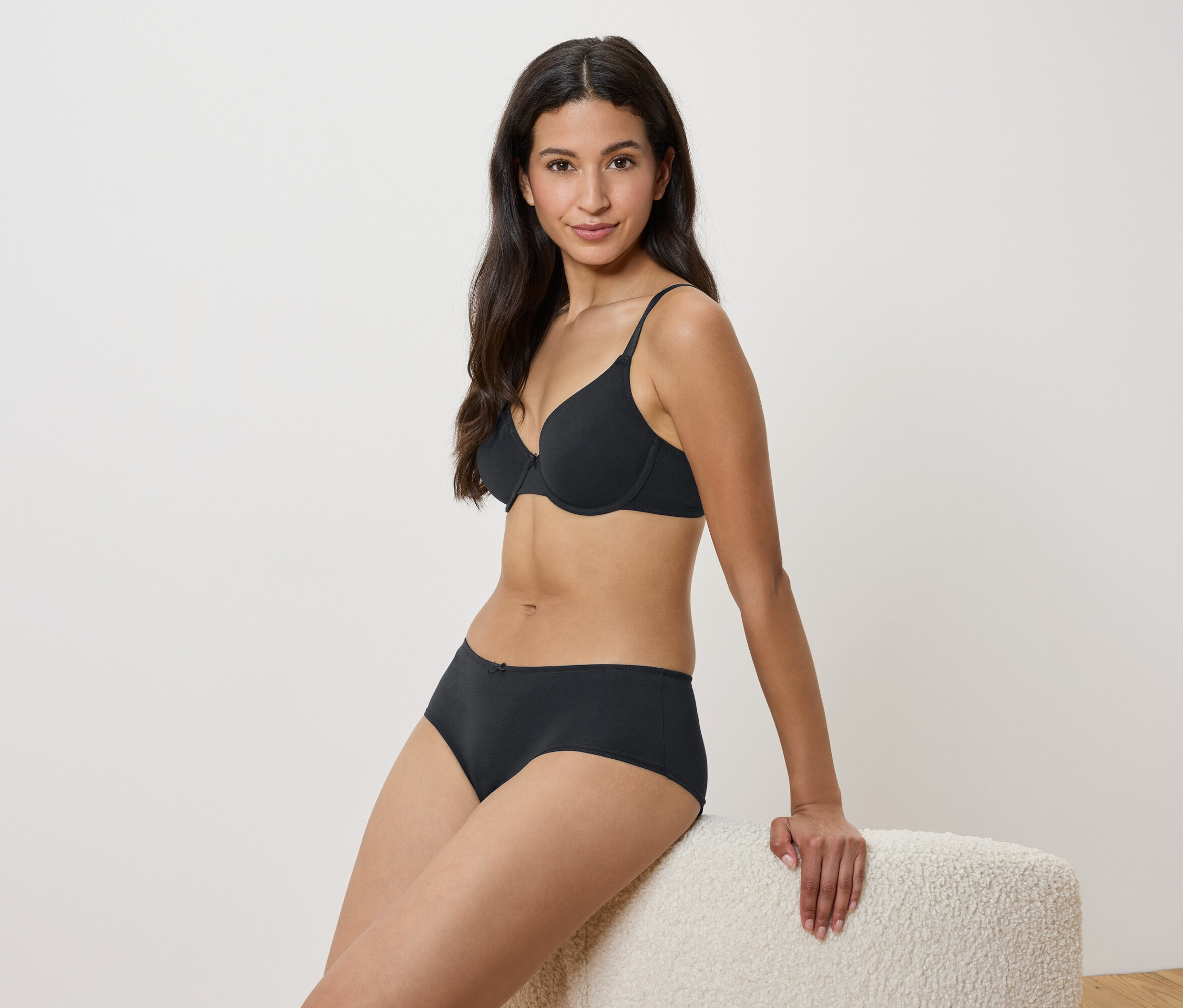 Kadın siyah sütyen ve külotla bir taburede oturuyor.