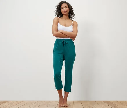 Bir kadın kolları çapraz bir şekilde duruyor ve yeşil bir pijama altı giyiyor.