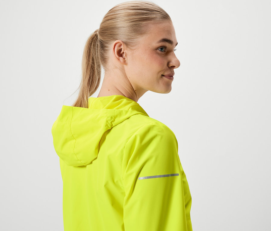 Sarışın saçları at kuyruğu yapılmış, neon sarısı kapüşonlu bir ceket giyen kadın.