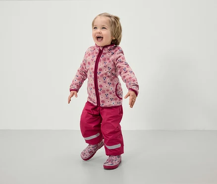 Çiçek desenli pembe polar ceket ve pembe pantolonlu küçük çocuk.