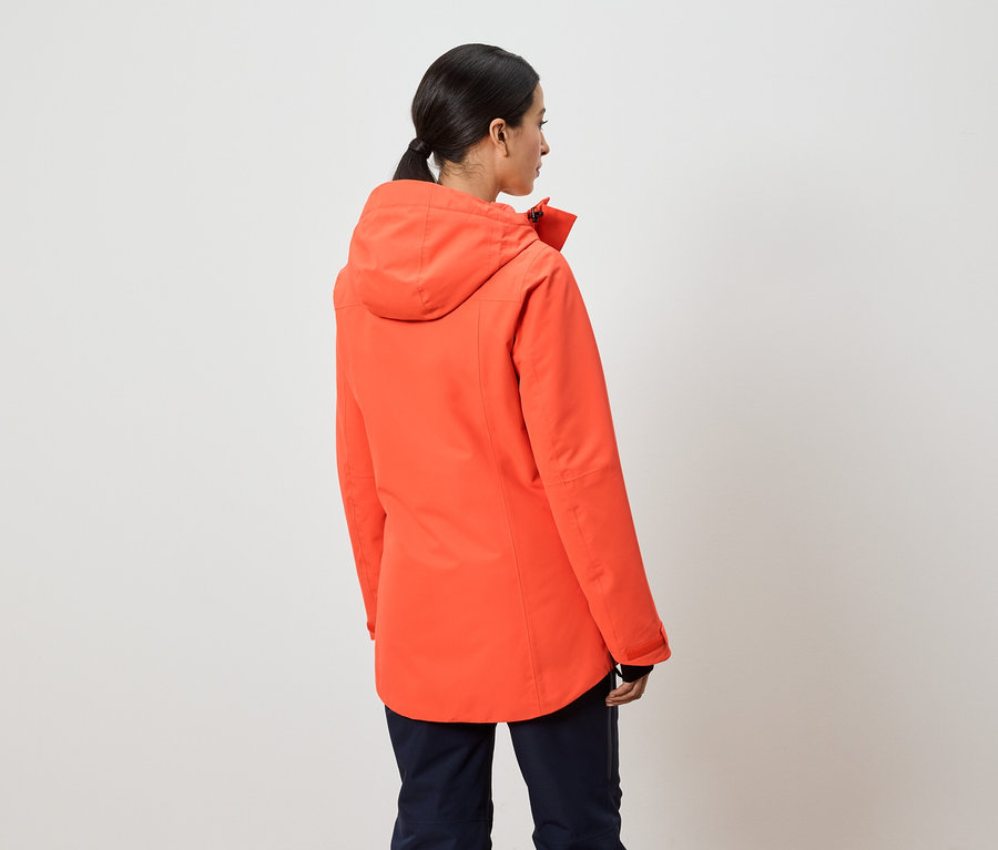 Sırtı kameraya dönük bir kadın, turuncu kapüşonlu bir ceket giyiyor.