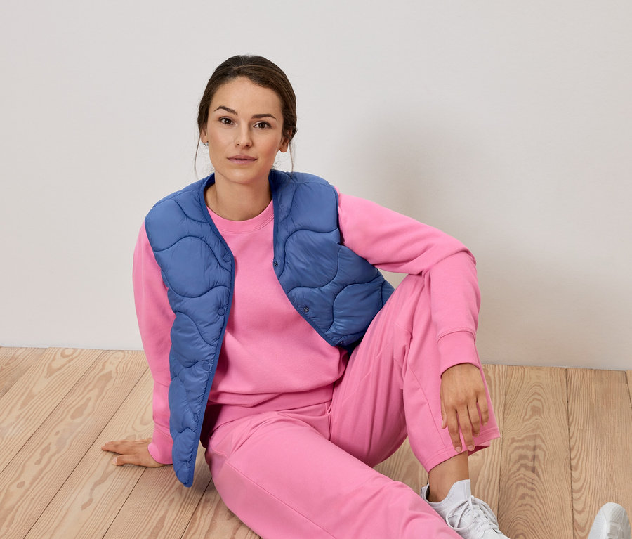 Kadın pembe eşofman ve mavi yelek ile yerde oturuyor.